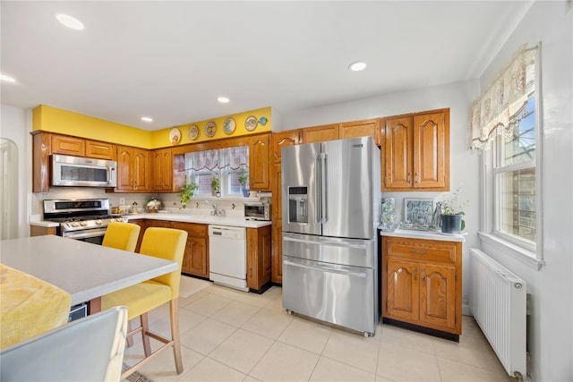 kitchen featuring radiator, appliances with stainless steel finishes, light tile patterned flooring, and sink