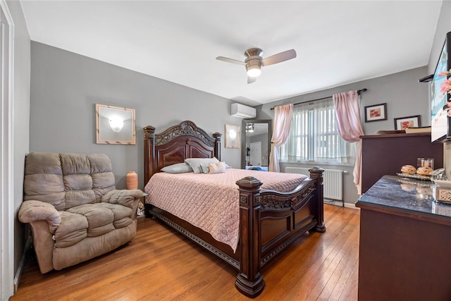 bedroom featuring ceiling fan, radiator, an AC wall unit, and hardwood / wood-style flooring