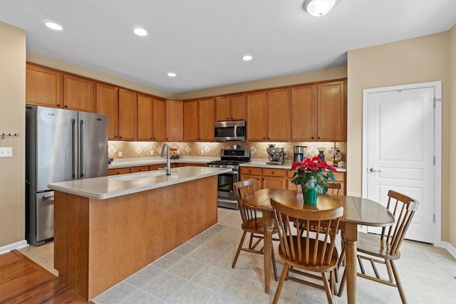 kitchen with sink, backsplash, appliances with stainless steel finishes, and a kitchen island with sink