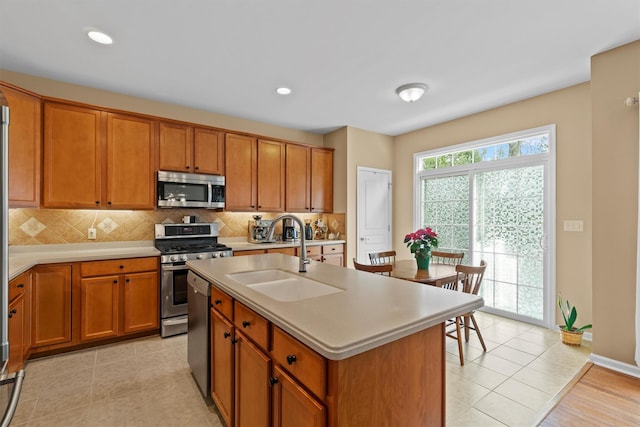 kitchen with decorative backsplash, sink, light tile patterned flooring, a kitchen island with sink, and stainless steel appliances