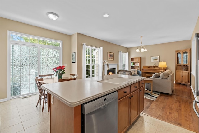 kitchen with a center island with sink, decorative light fixtures, light tile patterned flooring, stainless steel dishwasher, and sink