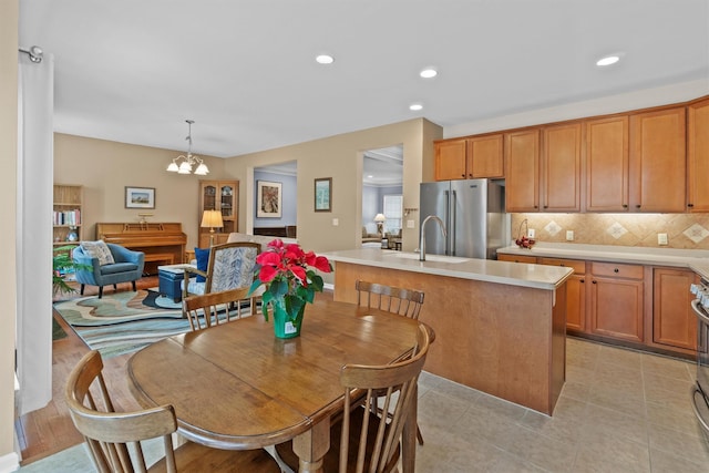 kitchen featuring decorative light fixtures, a notable chandelier, decorative backsplash, appliances with stainless steel finishes, and an island with sink