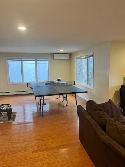 playroom with an AC wall unit, a baseboard heating unit, light hardwood / wood-style flooring, and a healthy amount of sunlight