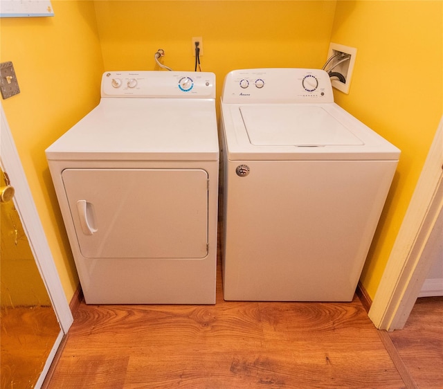 clothes washing area with washing machine and clothes dryer and light wood-type flooring