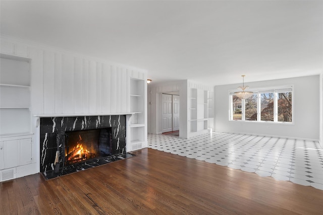 unfurnished living room featuring an inviting chandelier, hardwood / wood-style floors, built in shelves, and a high end fireplace