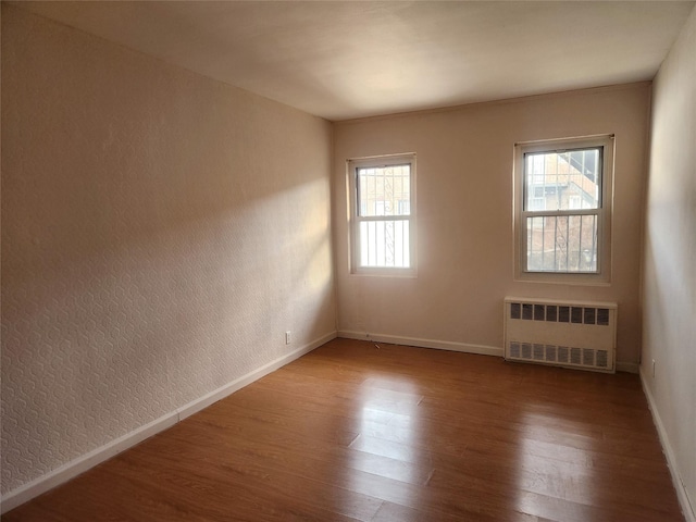 unfurnished room with radiator heating unit, hardwood / wood-style floors, and a wealth of natural light