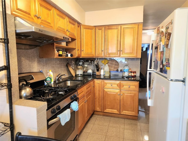 kitchen with sink, backsplash, stainless steel gas range oven, dark stone counters, and white fridge