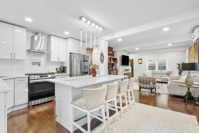 kitchen featuring wall chimney exhaust hood, white cabinets, a center island, and appliances with stainless steel finishes