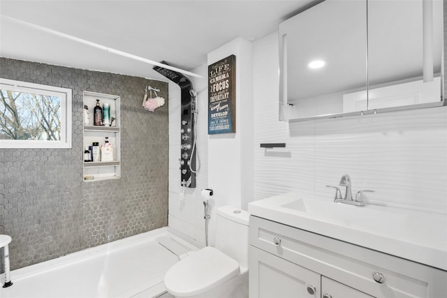 bathroom featuring vanity, backsplash, tile walls, toilet, and tiled shower