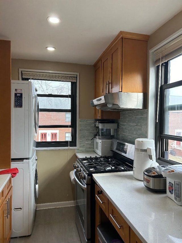 kitchen featuring stainless steel gas stove, a wealth of natural light, decorative backsplash, and stacked washer and dryer