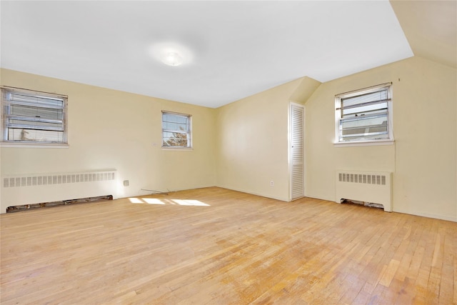 additional living space with radiator, lofted ceiling, and light wood-type flooring