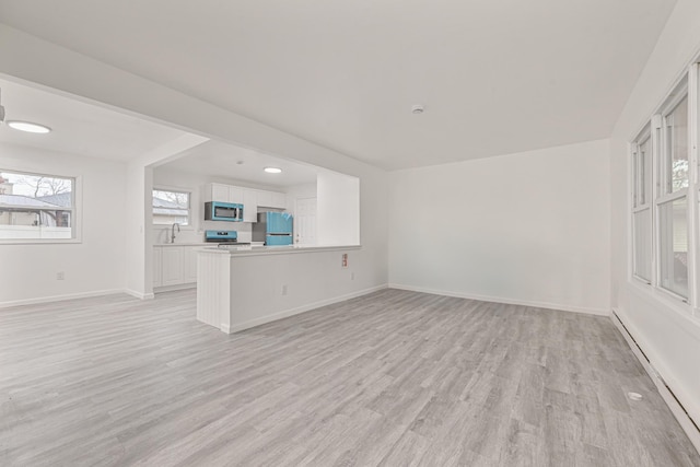 unfurnished living room with baseboard heating, sink, and light wood-type flooring