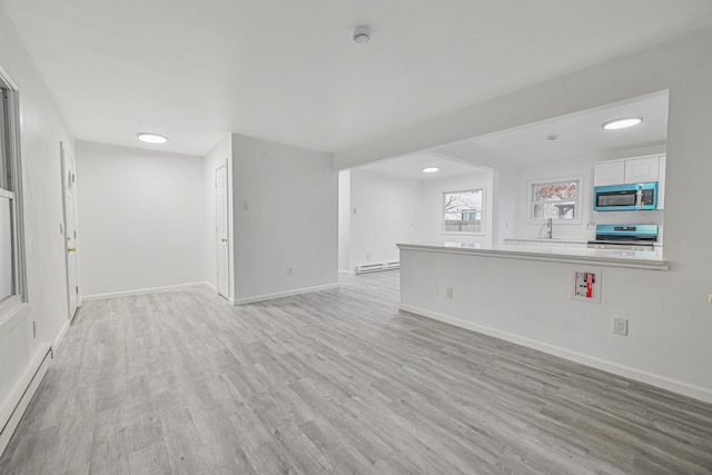 unfurnished room featuring light hardwood / wood-style floors, a baseboard radiator, and sink