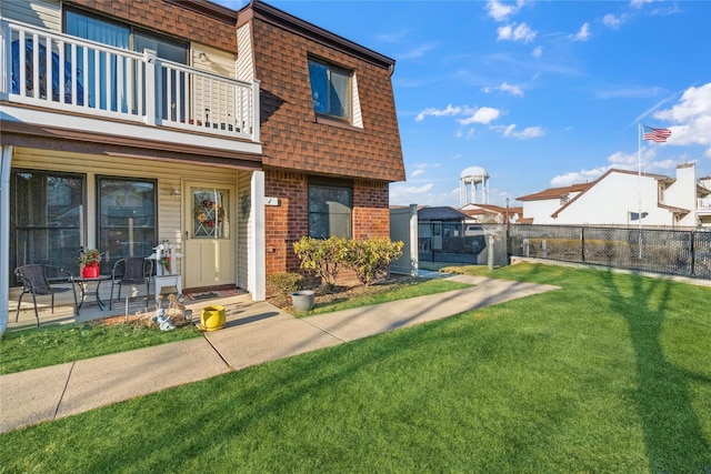 exterior space with mansard roof, a balcony, brick siding, a shingled roof, and fence