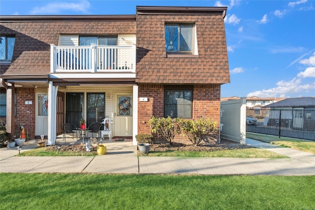 view of front of home featuring brick siding, mansard roof, roof with shingles, and a balcony