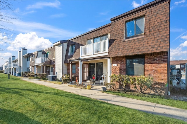 multi unit property with brick siding, roof with shingles, central AC unit, a balcony, and a front lawn