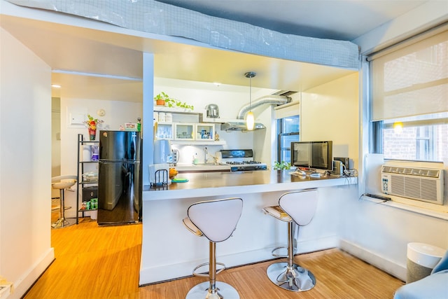 kitchen with light hardwood / wood-style floors, hanging light fixtures, black fridge, kitchen peninsula, and stove