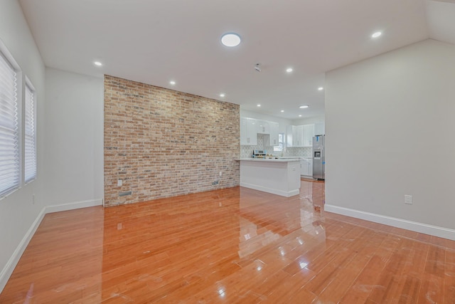 unfurnished living room with brick wall and light wood-type flooring