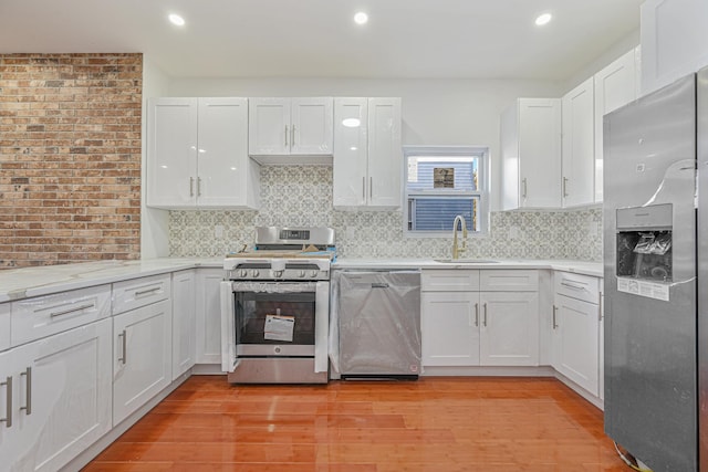 kitchen featuring appliances with stainless steel finishes, white cabinetry, tasteful backsplash, sink, and light wood-type flooring