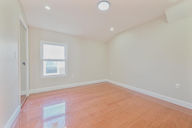 spare room featuring light wood-type flooring and vaulted ceiling