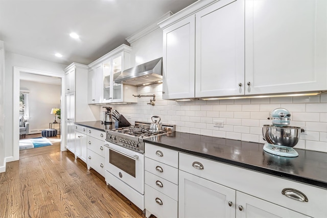 kitchen featuring dark wood finished floors, dark countertops, wall chimney exhaust hood, gas range oven, and white cabinetry