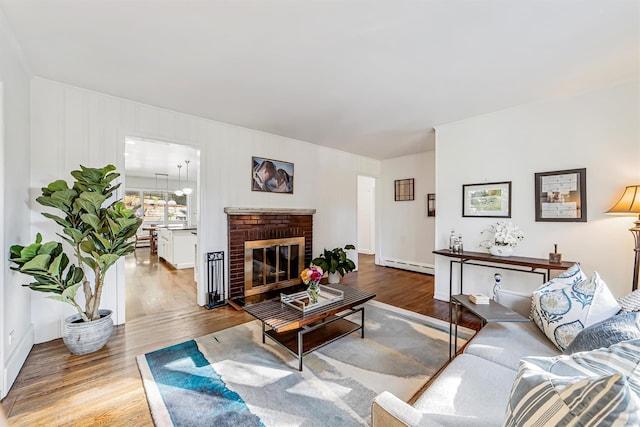 living room with a brick fireplace, baseboard heating, and wood finished floors