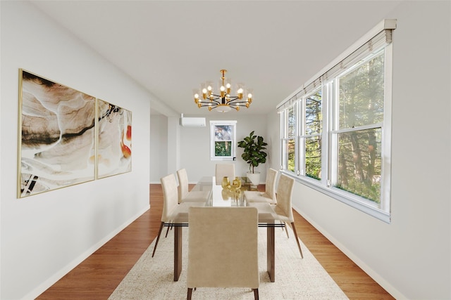 dining area featuring a chandelier, a wall unit AC, wood finished floors, and baseboards