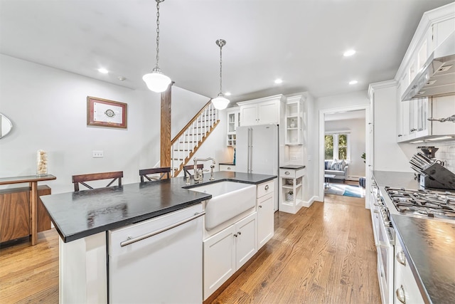 kitchen with dark countertops, white appliances, a sink, and wall chimney range hood