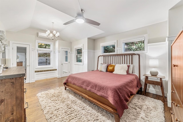 bedroom featuring multiple windows, vaulted ceiling, wood finished floors, and a wall mounted air conditioner