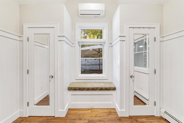 mudroom with a baseboard heating unit, light wood finished floors, a wall mounted air conditioner, and a decorative wall