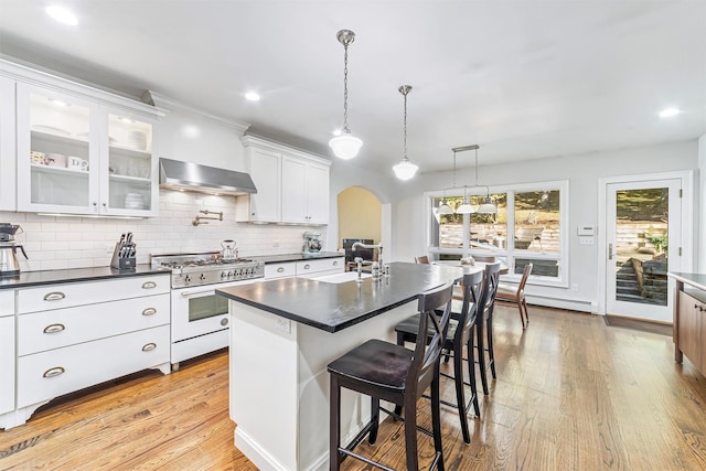 kitchen with range with gas stovetop, arched walkways, a breakfast bar area, dark countertops, and wall chimney range hood