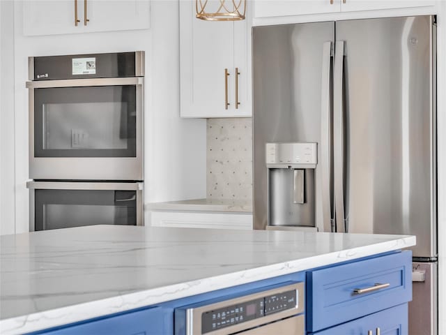 kitchen with light stone countertops, white cabinetry, stainless steel appliances, backsplash, and blue cabinets