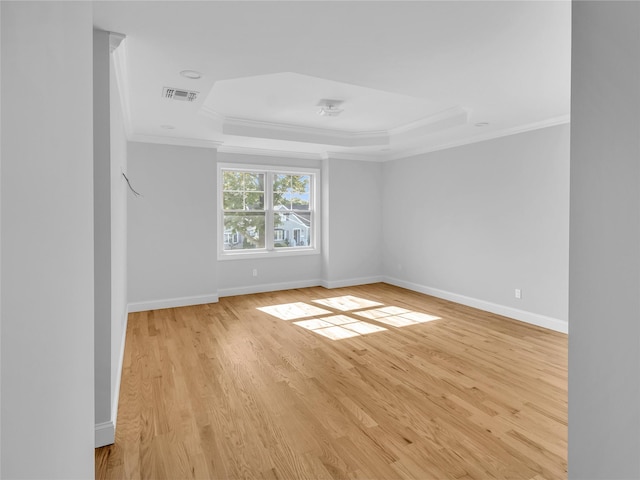 empty room with light wood-type flooring, a tray ceiling, and ornamental molding