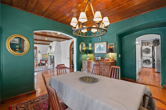 dining room featuring wood ceiling, stacked washer / drying machine, wood-type flooring, a chandelier, and beam ceiling