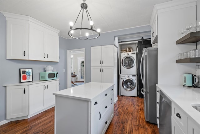 kitchen featuring stacked washer and clothes dryer, stainless steel appliances, pendant lighting, and white cabinets