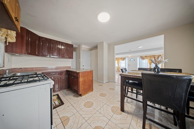 kitchen with a kitchen island, white range with gas cooktop, light tile patterned floors, and sink