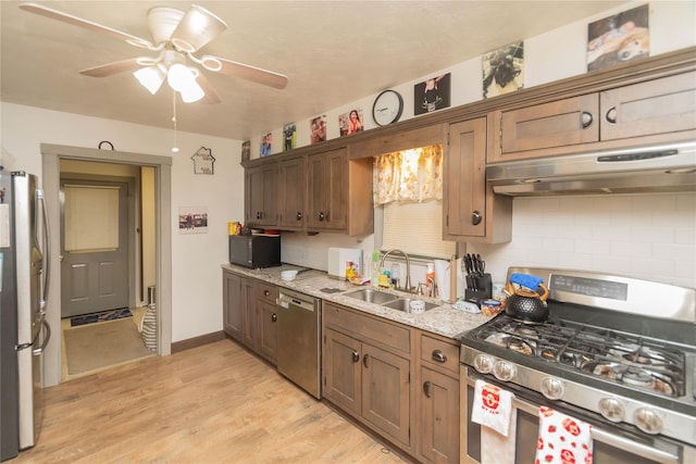 kitchen featuring appliances with stainless steel finishes, tasteful backsplash, light wood-type flooring, light stone countertops, and sink