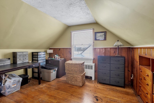 office space featuring radiator heating unit, wooden walls, wood-type flooring, a textured ceiling, and vaulted ceiling