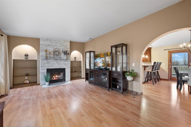 living room featuring light wood-type flooring, built in shelves, a stone fireplace, and a chandelier