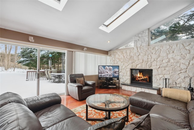 living room featuring light wood-type flooring, a stone fireplace, and vaulted ceiling with skylight