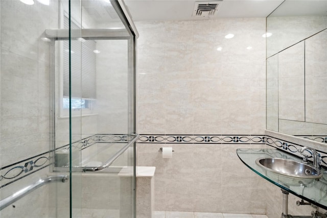 bathroom featuring sink, a shower with shower door, and tile walls