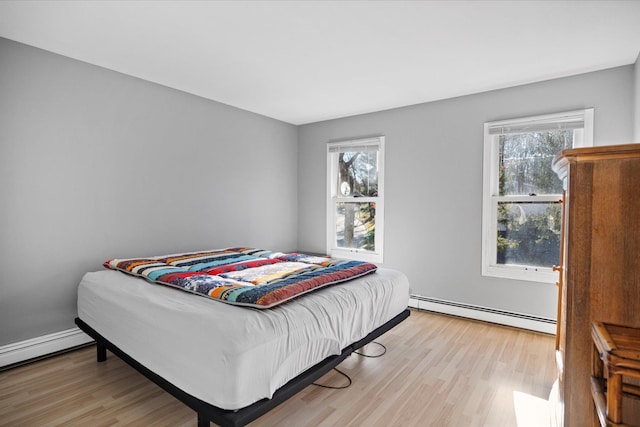 bedroom featuring a baseboard heating unit, light hardwood / wood-style flooring, and multiple windows