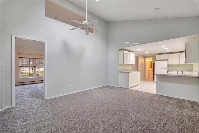 unfurnished living room featuring a towering ceiling, a baseboard heating unit, light carpet, sink, and ceiling fan