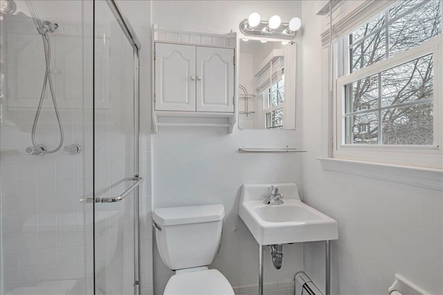 bathroom with a shower with shower door, sink, toilet, and a baseboard heating unit