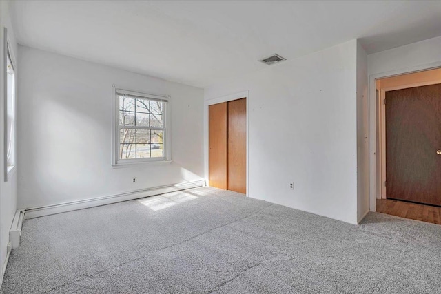 carpeted empty room featuring a baseboard heating unit