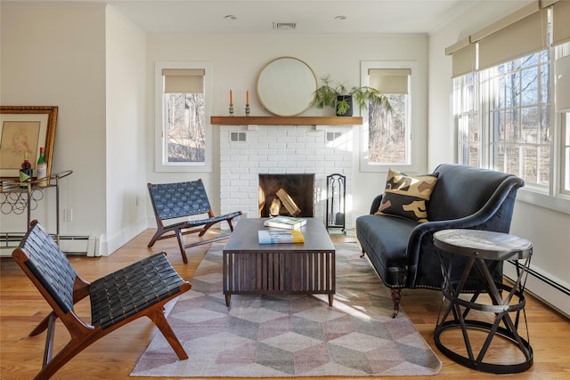 sitting room with a baseboard heating unit, ornamental molding, a fireplace, and light hardwood / wood-style flooring