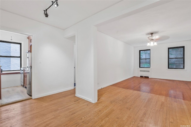 empty room featuring ceiling fan, radiator, a healthy amount of sunlight, and light hardwood / wood-style flooring