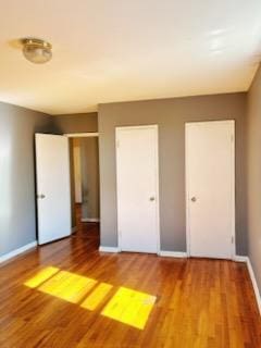 unfurnished bedroom with two closets and hardwood / wood-style floors