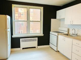 kitchen featuring backsplash, sink, white appliances, radiator, and white cabinets