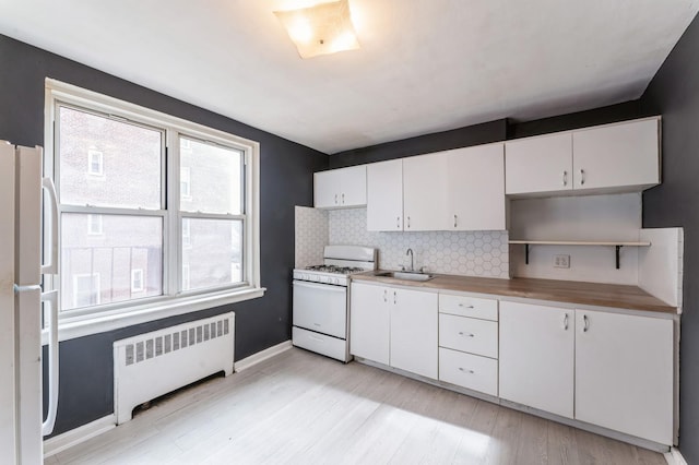 kitchen with radiator, white appliances, white cabinetry, and a sink